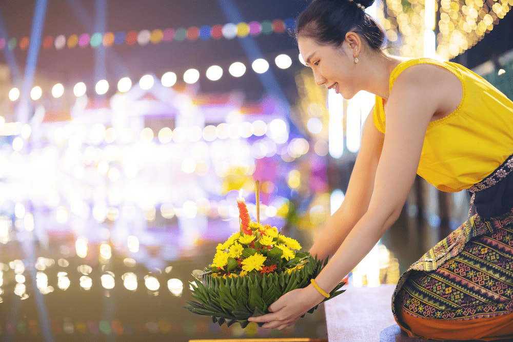 A woman lowering a krathong into the river during Loy Krathong in Nonthaburi.